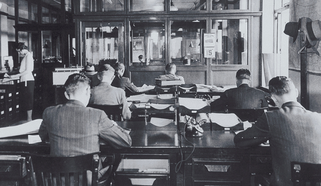 Black and white photo of men sitting in a room at desks